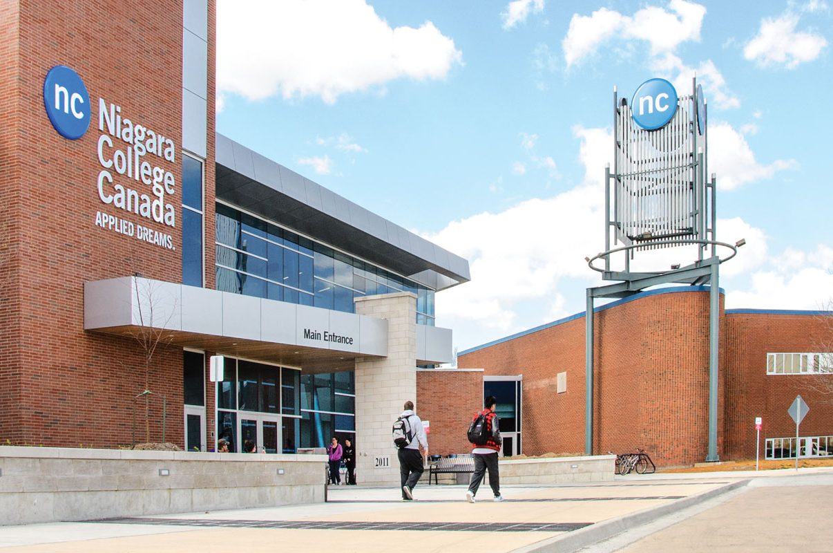 People walk towards the main entrance of Niagara College Canada, with the college sign and tower visible.