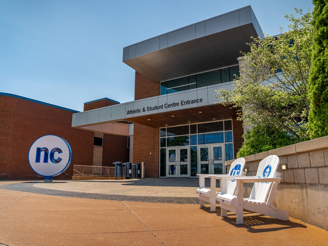 Entrance to the Athletic & Student Centre featuring benches and the Niagara College logo outside a modern brick building.