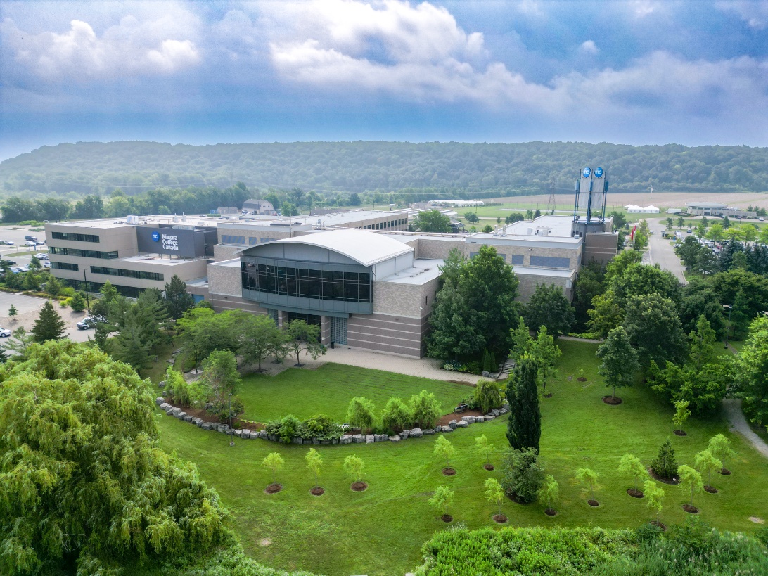 A large modern office building stands among trees and landscaped greenery, set against hills in the background.