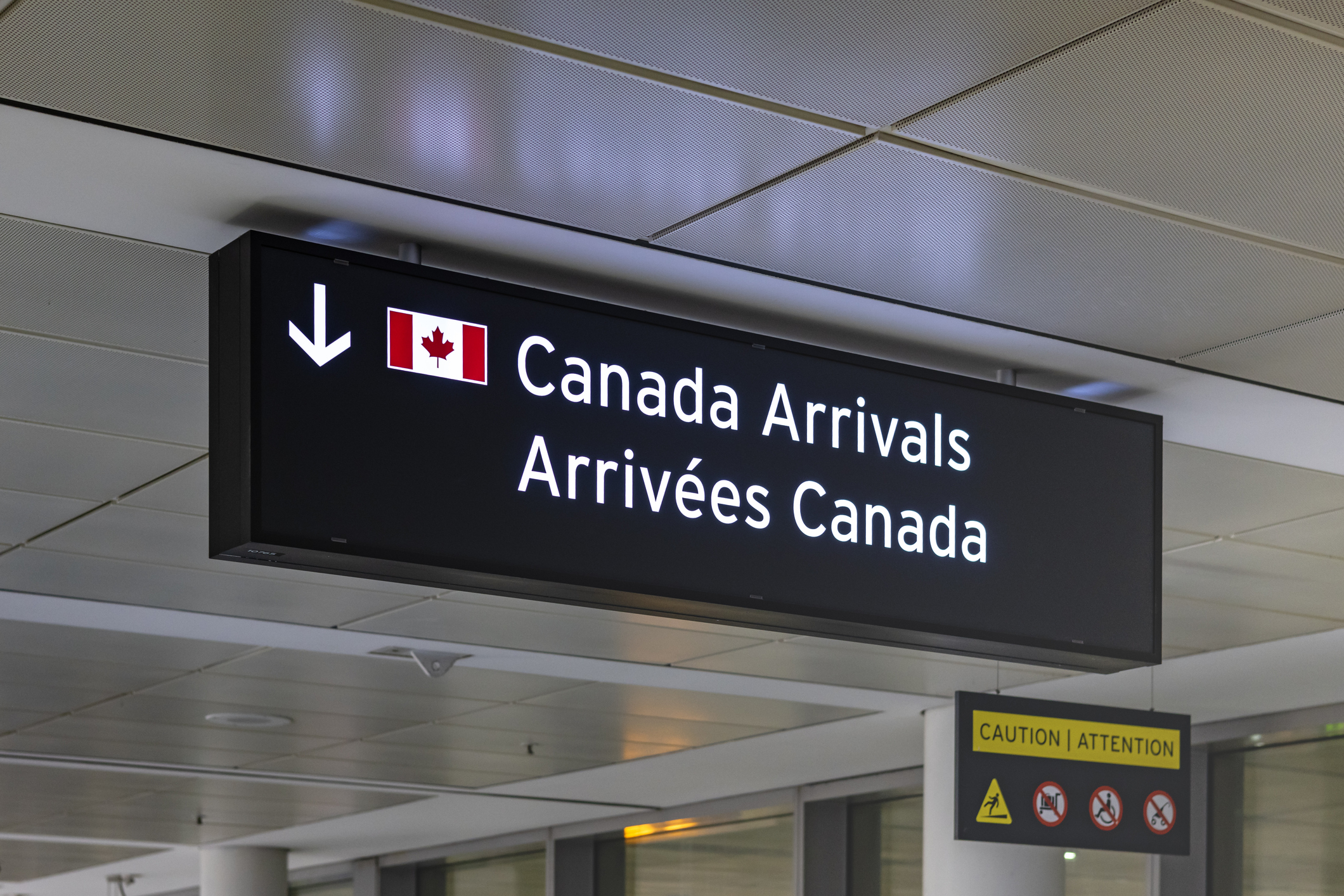 Bilingual sign displaying “Canada Arrivals / Arrivées Canada” alongside a Canadian flag in an airport terminal.