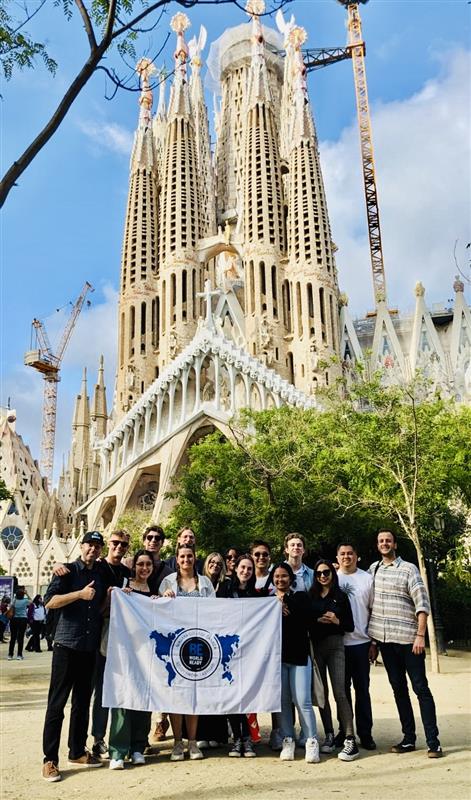 A group of individuals hold a white flag in front of the Sagrada Familia in Barcelona, Spain, on a sunny day.