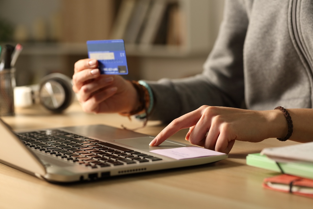 Individual holding a credit card and using a laptop, possibly making an online purchase or entering payment details.