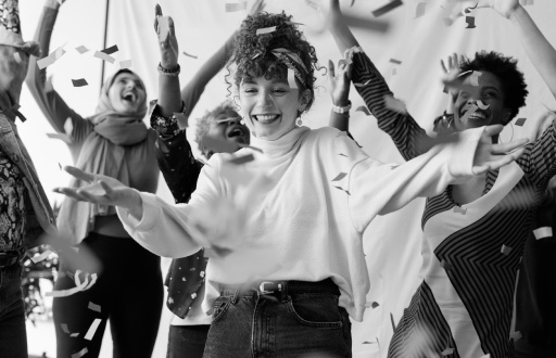 A woman dancing and smiling among friends as confetti falls around them.